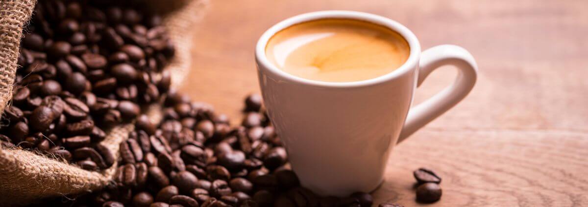 Weiße Espressotasse, die neben einem Beutel mit Kaffeebohnen steht.