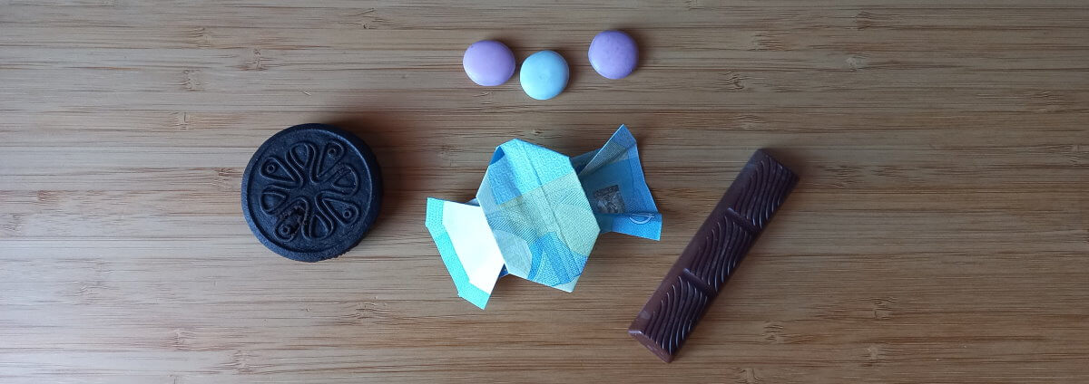 Bonbon aus Geldschein falten. Dieses Geldgeschenk liegt zwischen anderen Süßigkeiten.
