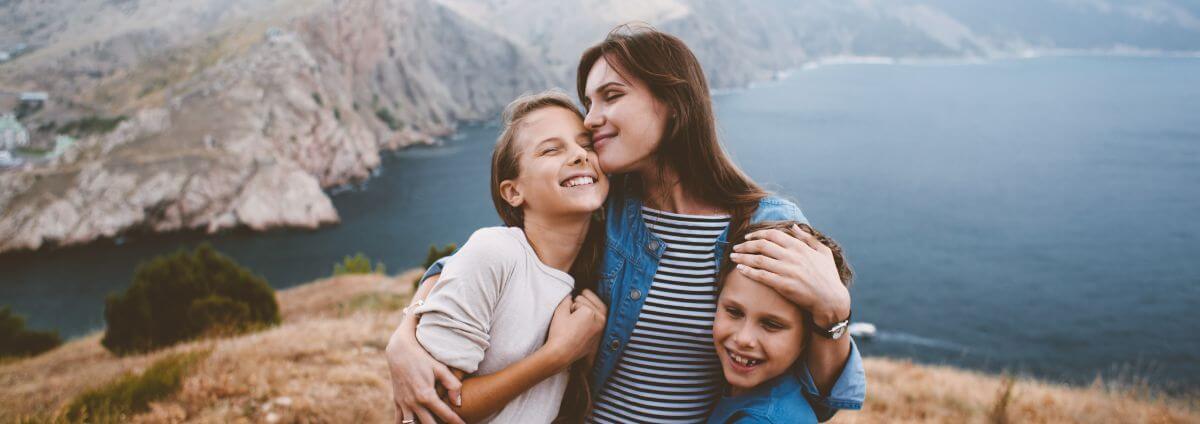 Mutter mit ihren Kindern, die gemeinsam an einer Klippe stehen und sich umarmen.
