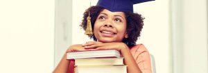 Studentin aufgestützt auf einem Bücherstapel. Geschenke zum Bachelor.