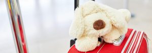 Weißer Kuscheltierhund, der auf einem roten Koffer liegt.
