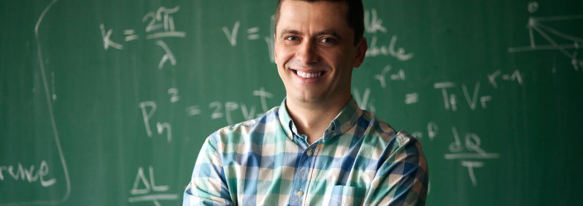 Mann, der vor einer Tafel steht, auf der mathematische Formeln stehen.