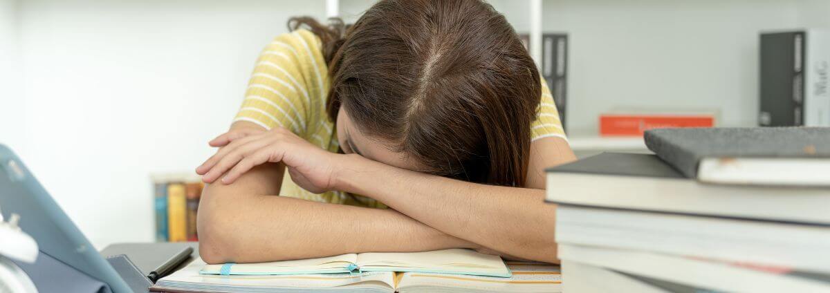 Studentin, die ihren Kopf auf ein Lehrbuch gelegt hat.