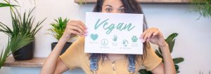Frau, die ein Schild mit dem Schriftzug "vegan" hochhält.