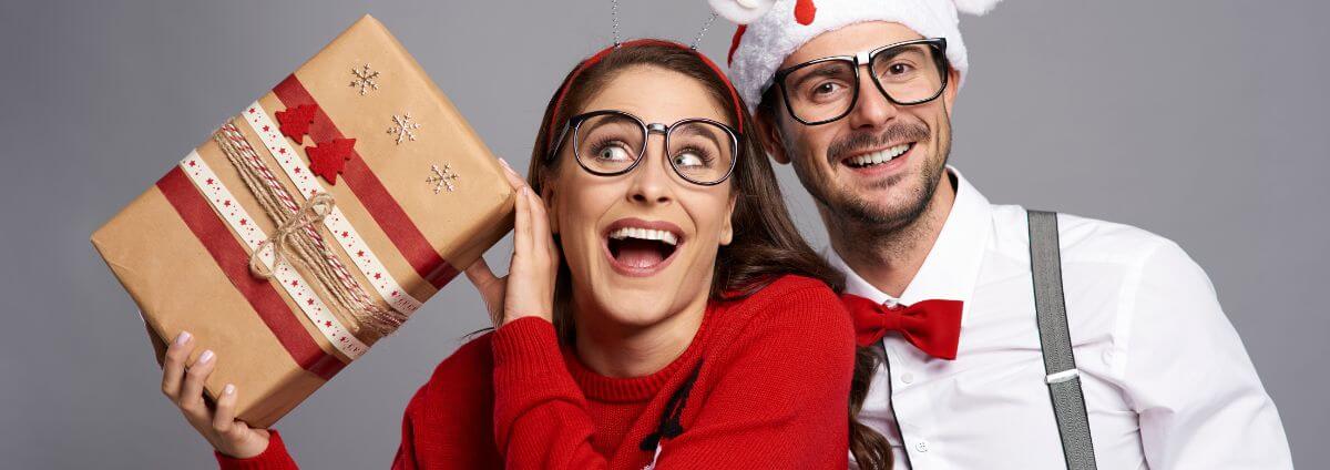 Eine Frau und ein Mann, die ein witziges Weihnachtsoutfit anhaben und ein Geschenk in der Hand halten.