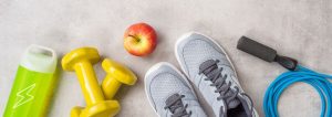 Turnschuhe, Trinkflasche, Hanteln, Springseil und ein Apfel als Sinnbild für Fitness.